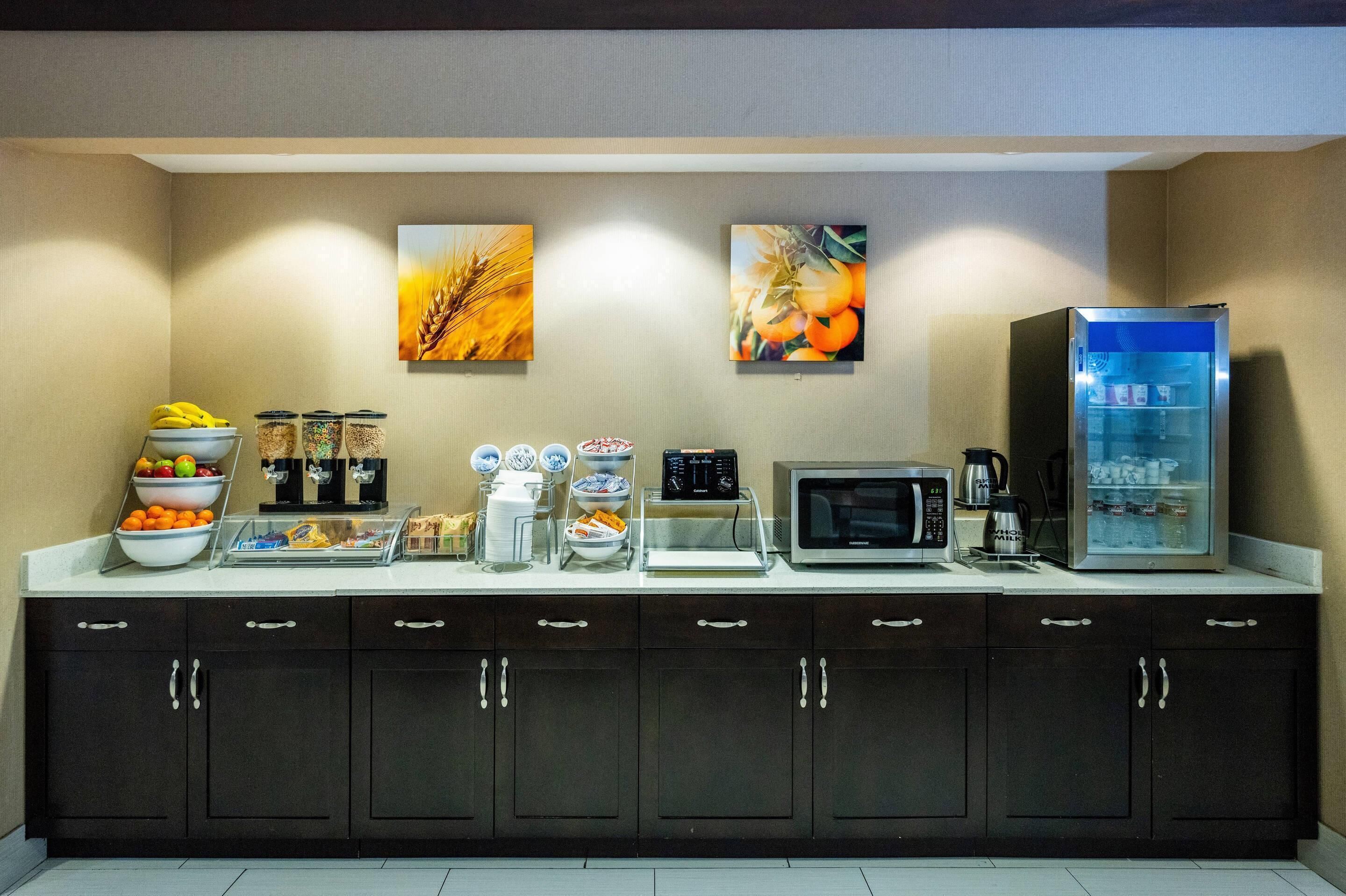 A kitchenette with a microwave, coffee maker, and refrigerator. There are bowls of fruit and condiments on the counter.