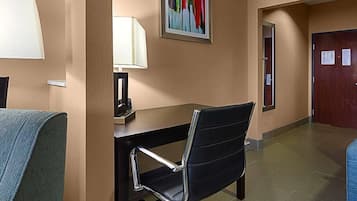 Una habitación de hotel con escritorio, silla, lámpara, obras de arte y una puerta.