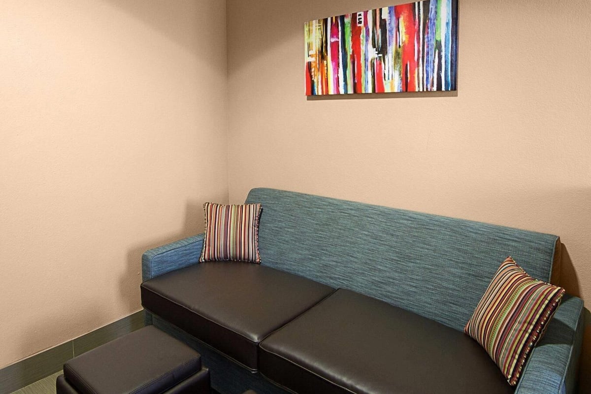 A corner seating area with a blue sofa, two striped pillows, and a black ottoman.