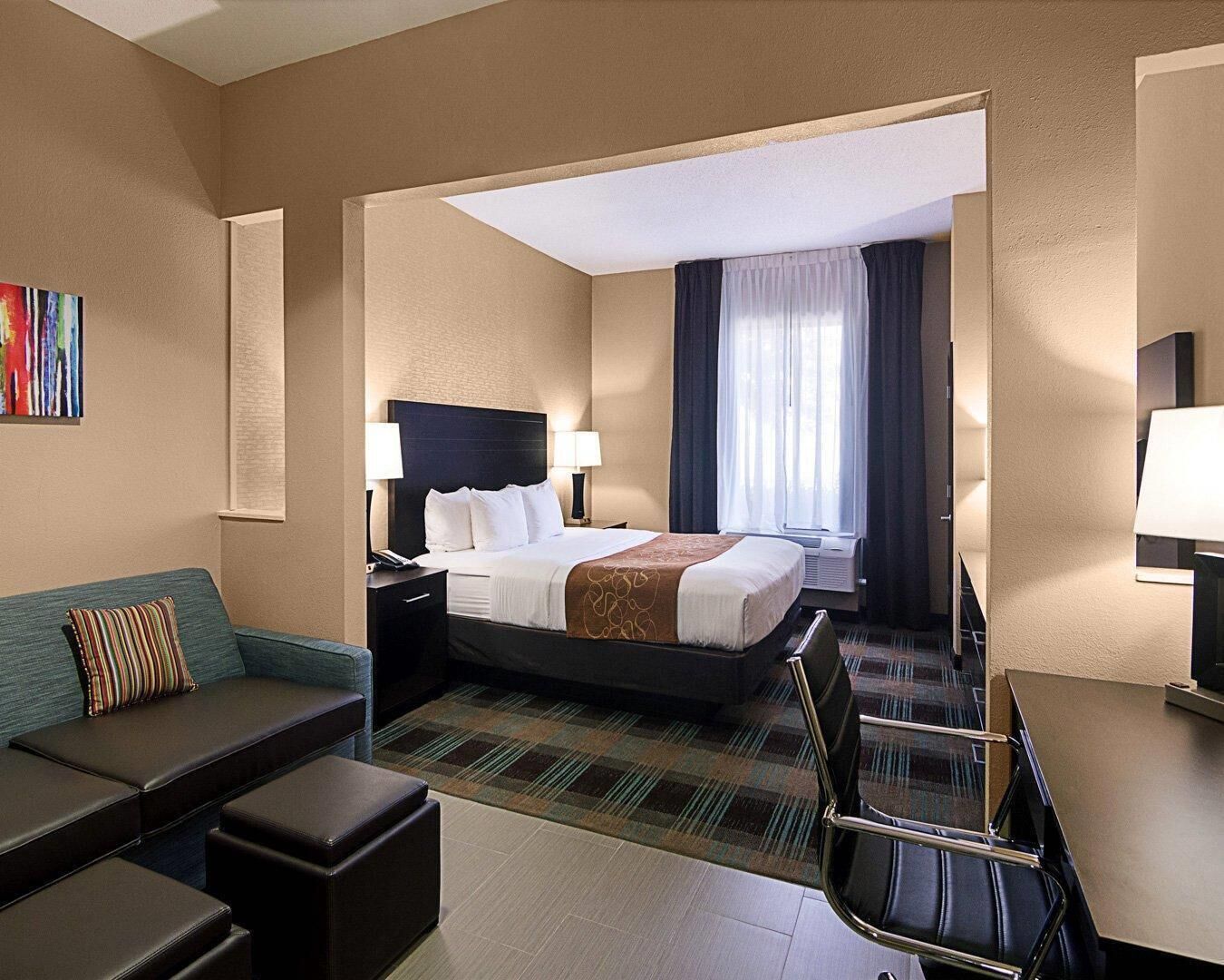 A hotel room with a bed, bedside tables, a desk, a chair, a sofa, and a window with curtains.