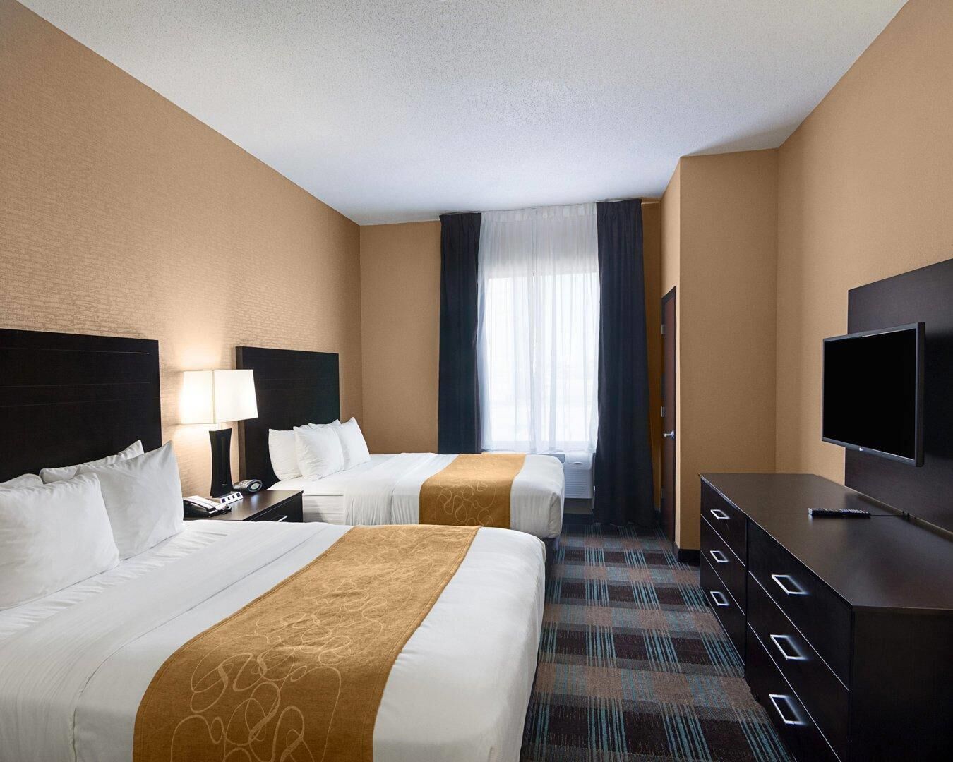 Quarto de hotel com duas camas, televisão, escrivaninha e janela com cortinas.