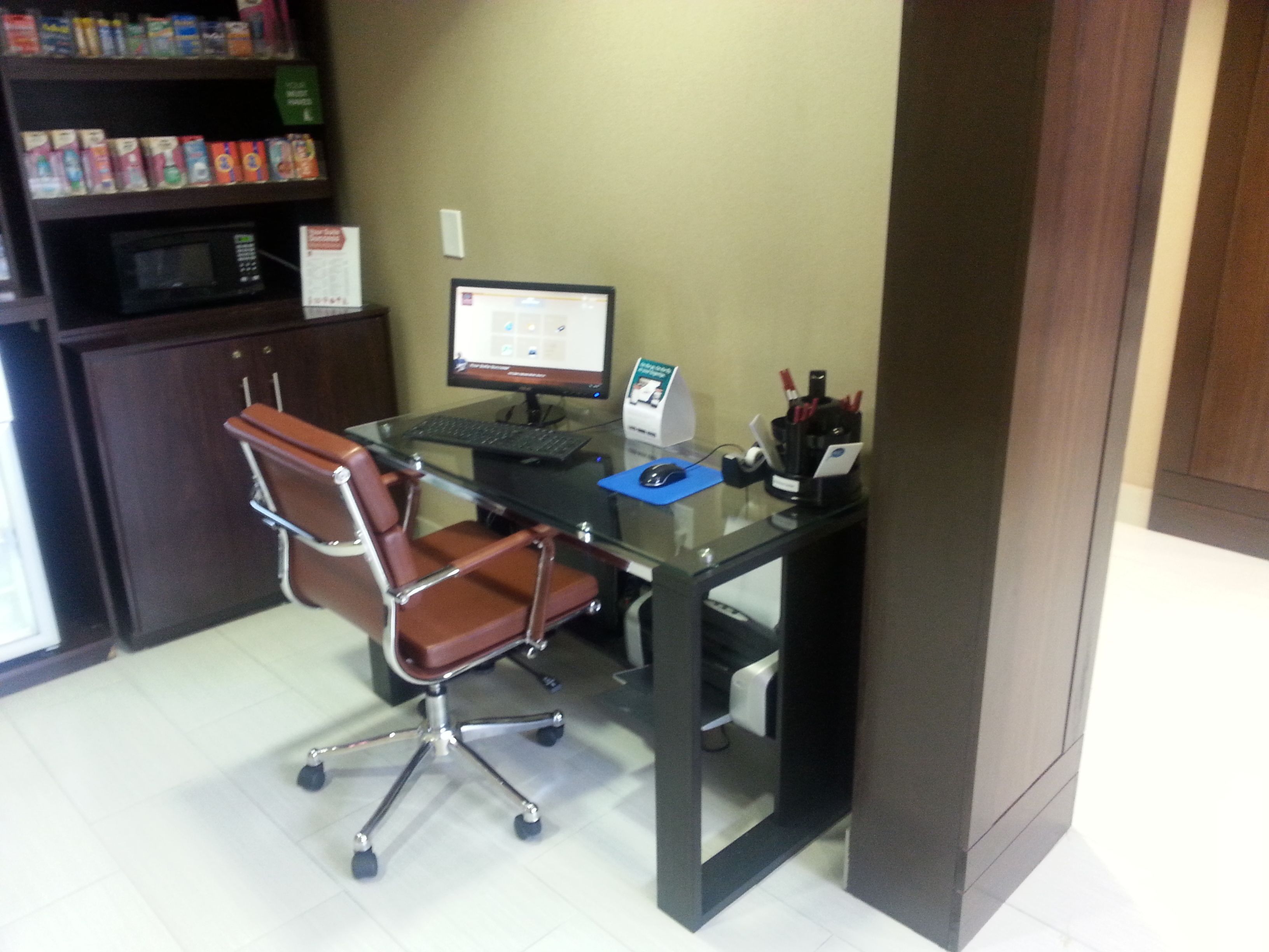 Un petit bureau équipé d’un bureau, d’un ordinateur, d’une chaise et d’étag ères où sont exposés des produits.