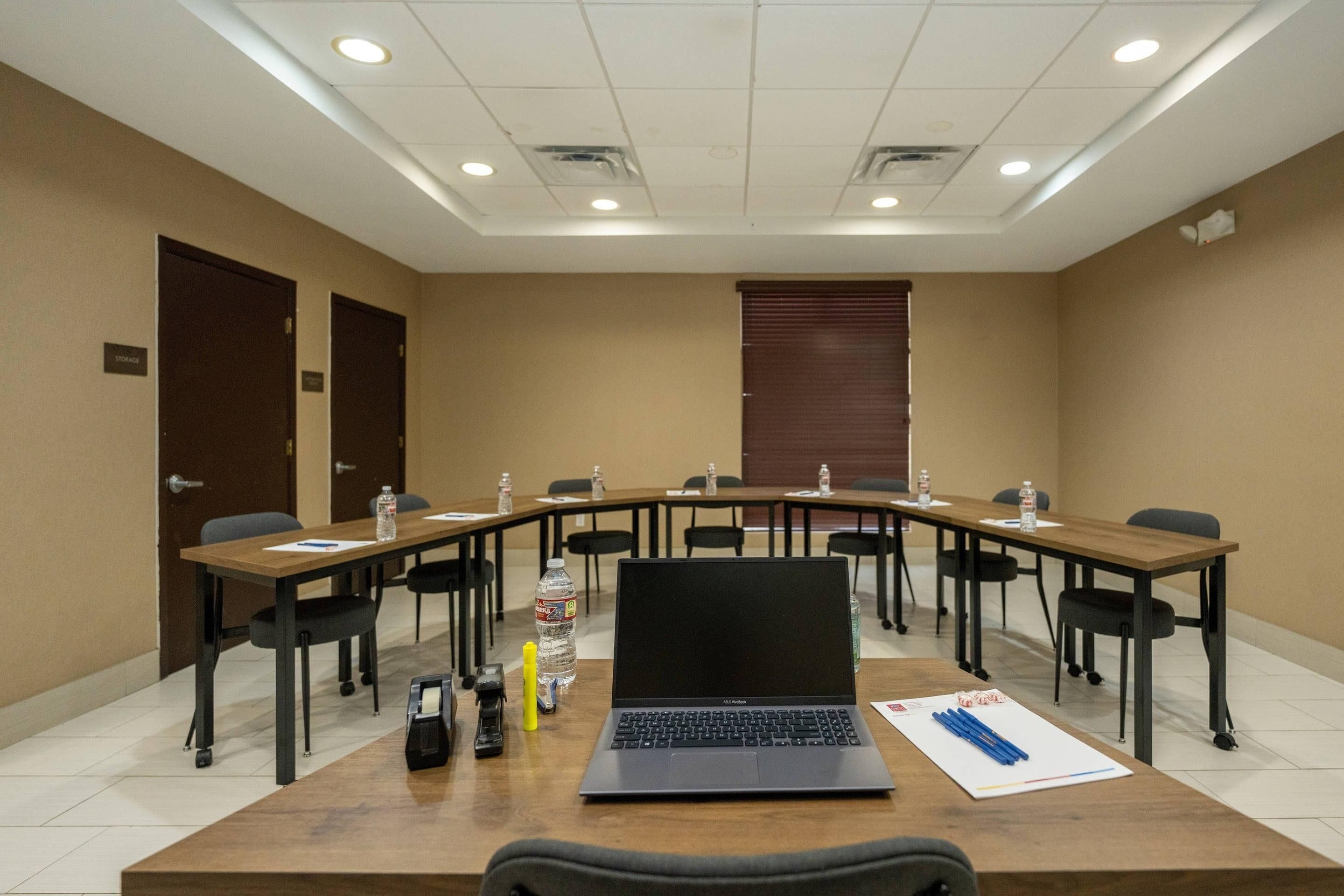 A conference room with a long table, chairs, a laptop, water bottles, and a door labeled 'STORAGE'.