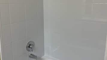 Une salle de bain avec des carreaux blancs, une baignoire et un espace douche.