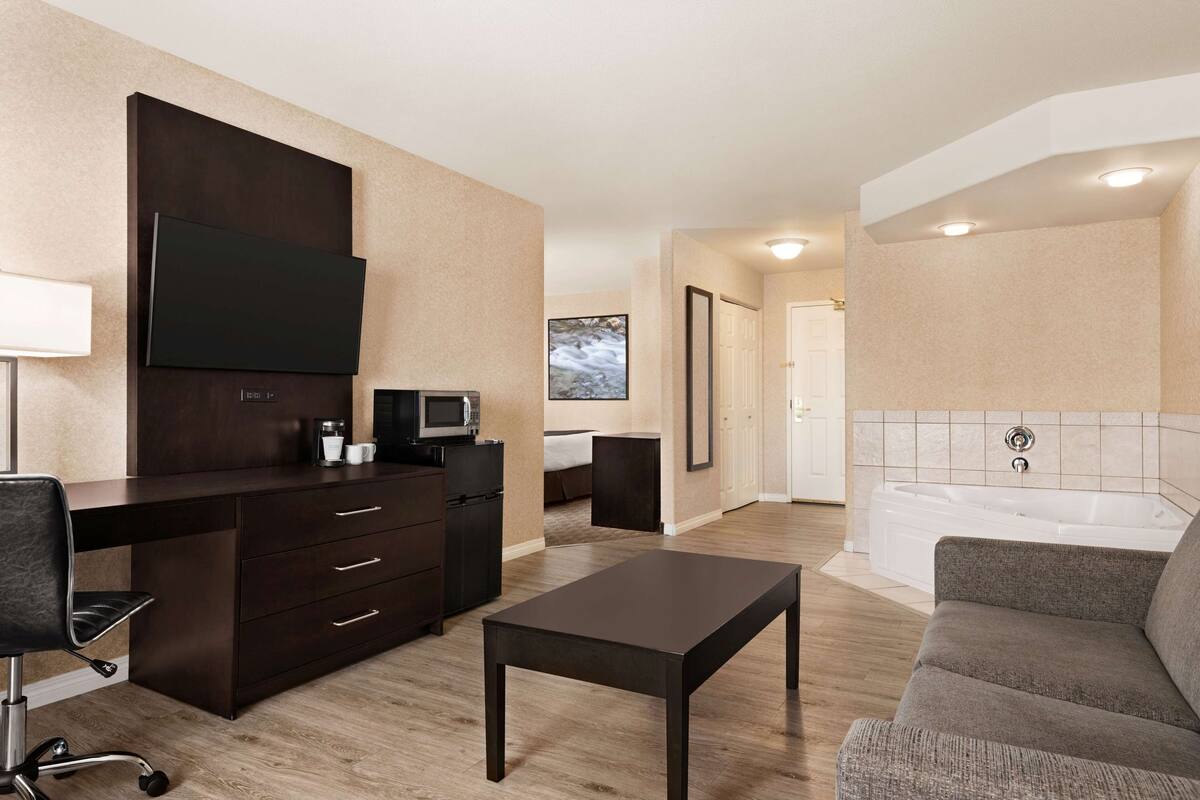 Una habitación de hotel moderna con un escritorio de madera oscura, un televisor de pantalla plana, un sofá, una mesita pequeña y una bañera.
