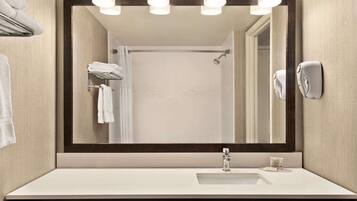 A modern bathroom with a large mirror, white sink, towel rack, and a handheld showerhead.