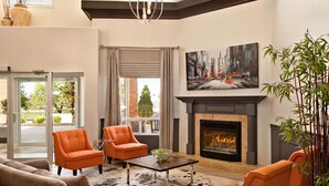 Un salon moderne avec une cheminée, des fauteuils orange, un canapé et un grand tableau.