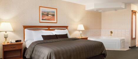 Habitación de hotel con una cama grande, dos mesitas de noche con lámparas, un cuadro en la pared y un baño independiente con bañera.