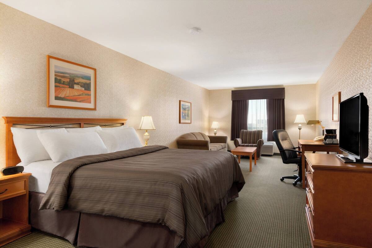 Habitación de hotel con una cama grande, un escritorio con computadora, una silla, un televisor y dos lámparas.