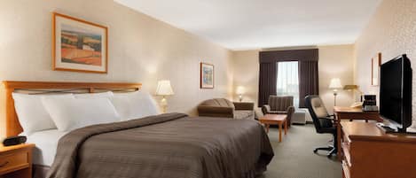 Habitación de hotel con una cama grande, un escritorio con computadora, una silla, un televisor y dos lámparas.
