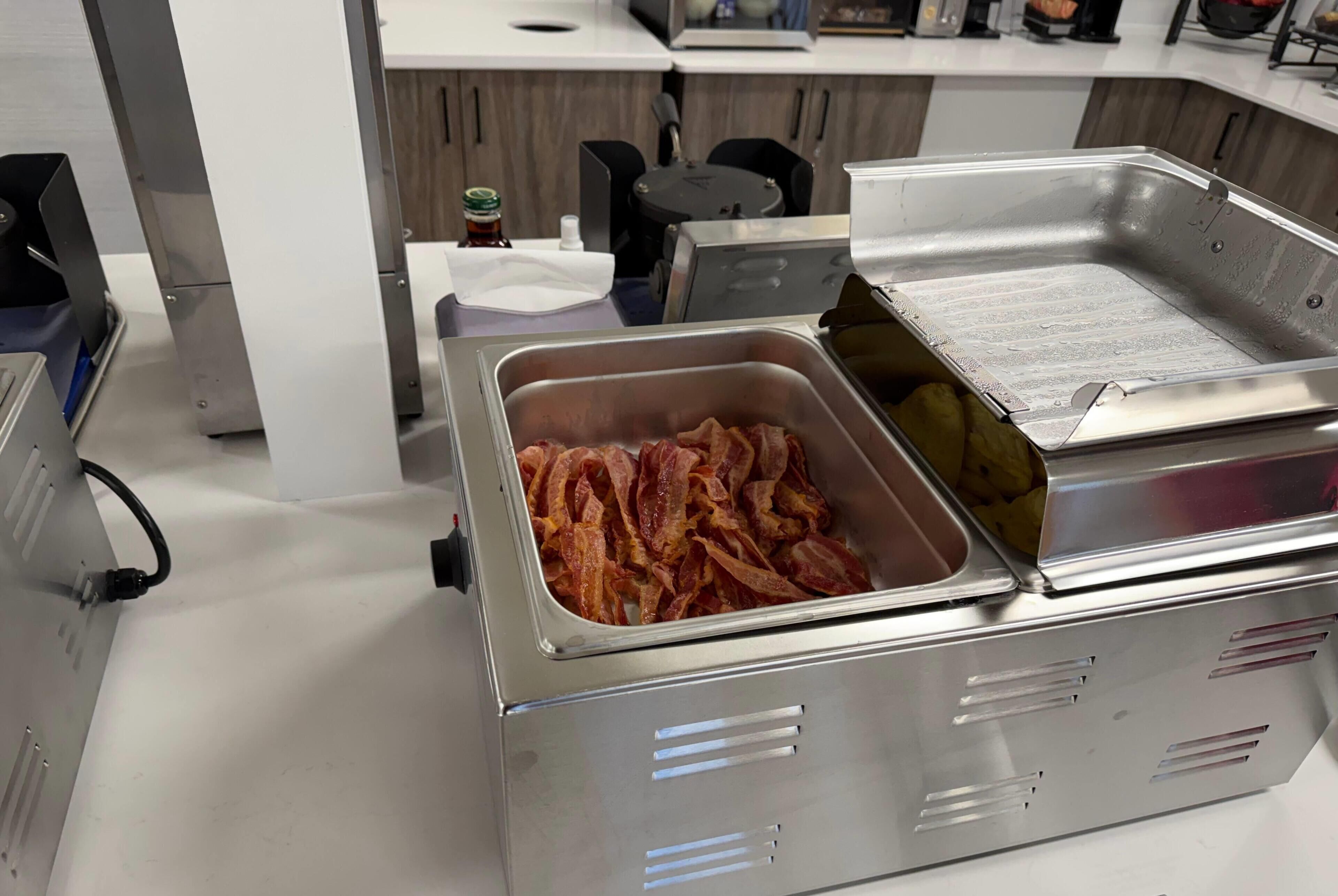 Eine Küchenzeile mit einer Speisevorbereitungsstation, darunter ein Tablett Speck und eine Fritteuse.