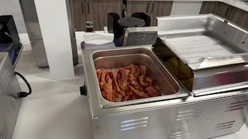 Eine Küchenzeile mit einer Speisevorbereitungsstation, darunter ein Tablett Speck und eine Fritteuse.