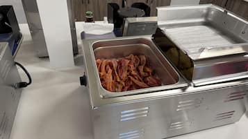 A buffet station with a container of bacon and a sign indicating 'Cheese and Veg Omelette.'