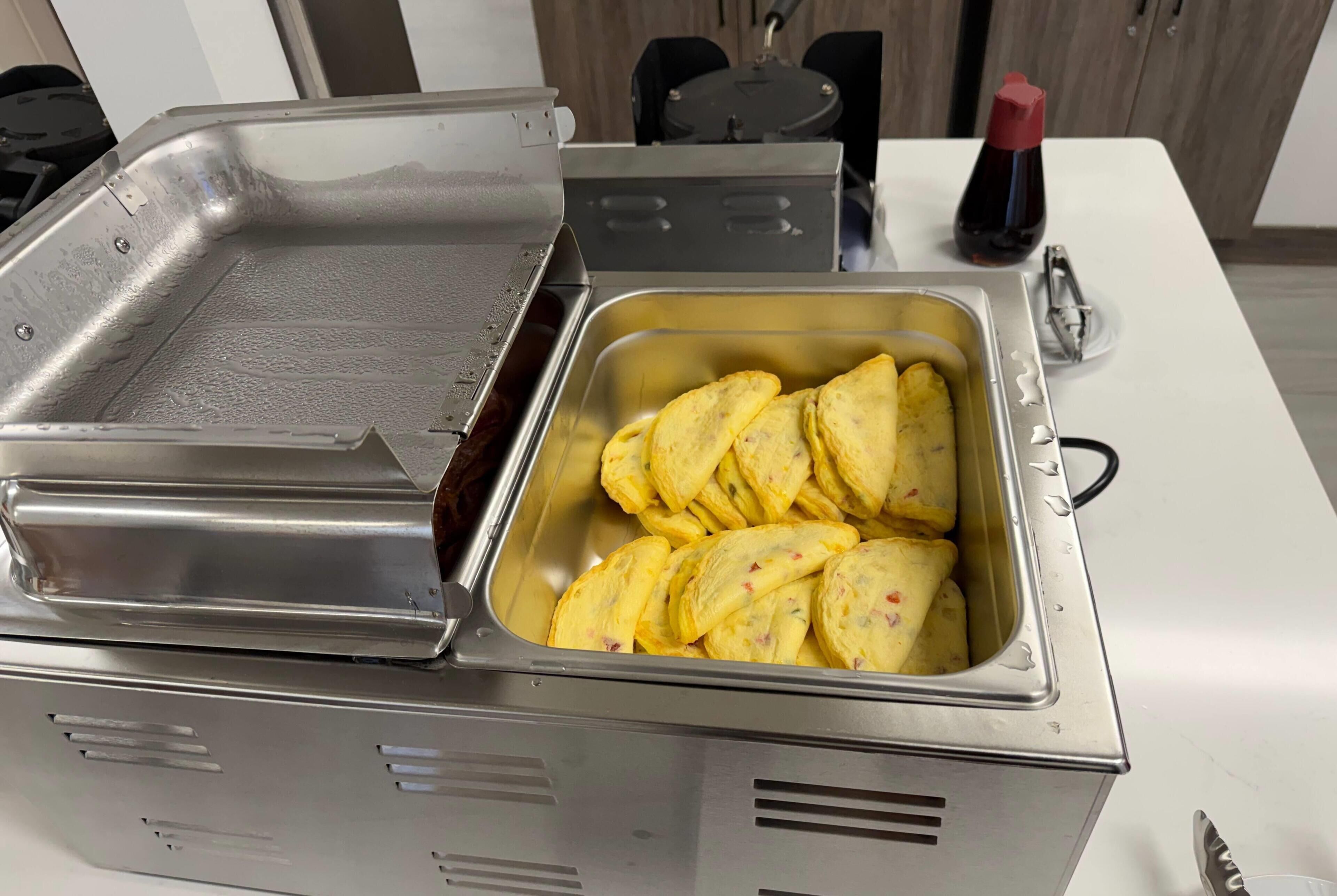 A kitchen with a deep fryer, a sink, and a bottle of sauce.