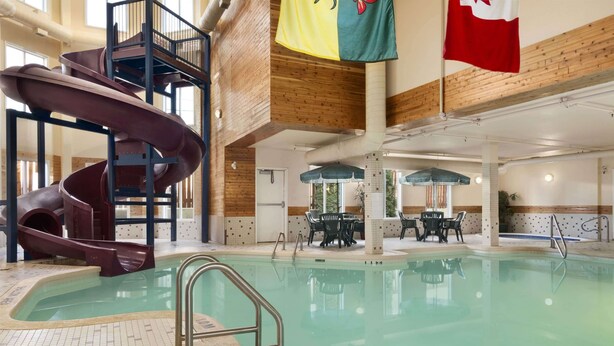 Une piscine avec un toboggan, une table et des chaises, et des drapeaux.