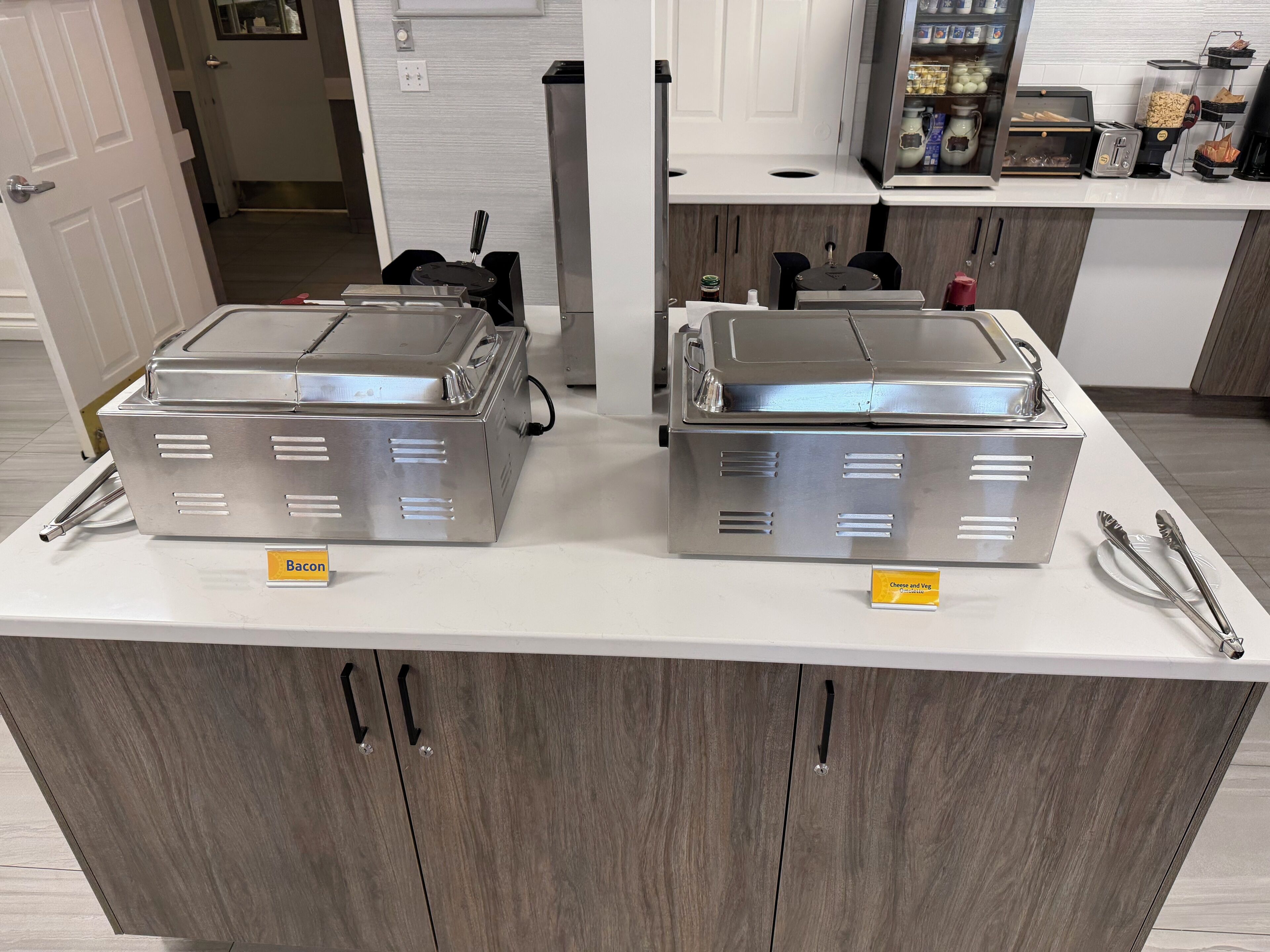 A buffet setup with two stainless steel chafing dishes labeled 'Bacon' and 'Cheese and Veg.'
