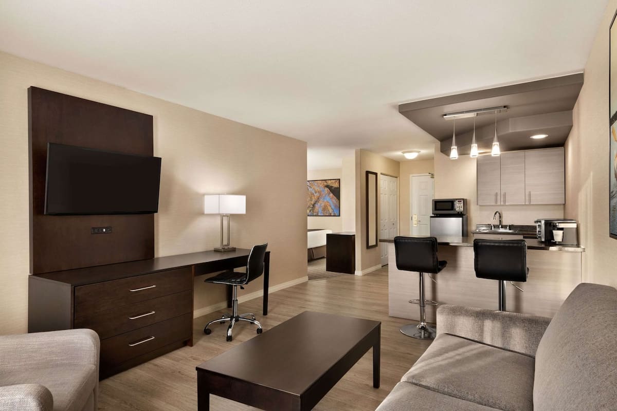 Una habitación de hotel moderna con una televisión de pantalla plana, un escritorio con una silla, un sofá, una mesa de centro y una kitchenette.