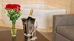 Une pièce avec une baignoire, un vase rempli de roses rouges, une bouteille de champagne dans un seau en métal et deux coupes à champagne posées sur une table.