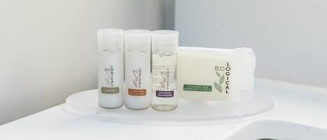 Um banheiro com bancada branca exibindo três frascos de produtos L'ECOLYGE e uma barra de sabão.