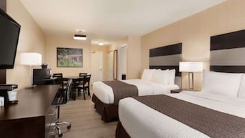 A hotel room with two beds, a desk, a television, and a dining area.