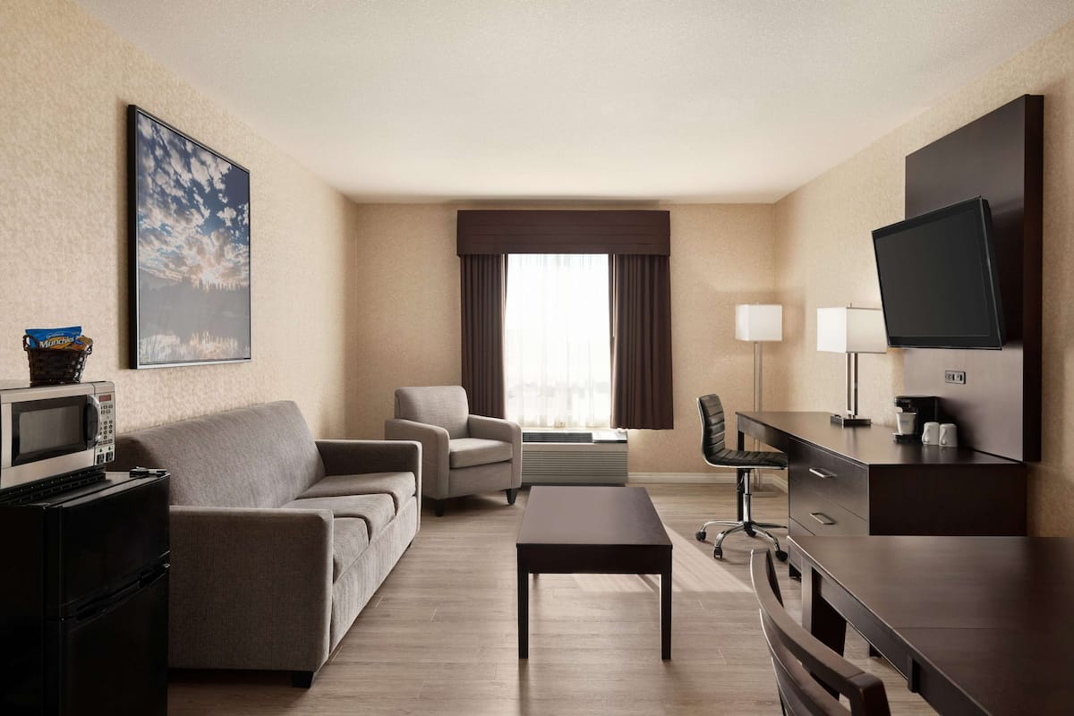 Habitación de hotel con sofá, sillón, televisor, escritorio y un amplio ventanal con cortinas.