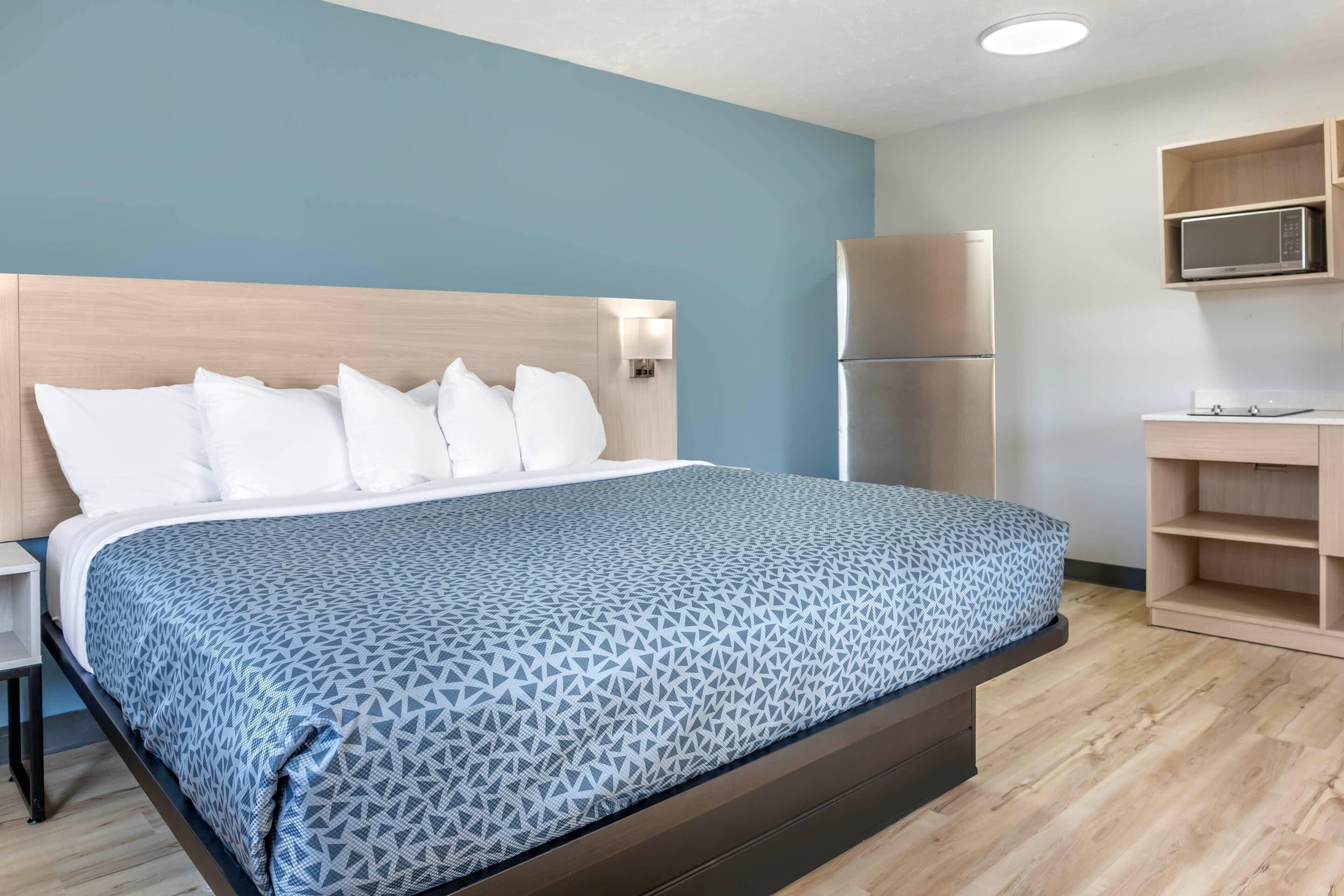 A hotel room with a bed, a nightstand, a microwave, and a refrigerator.