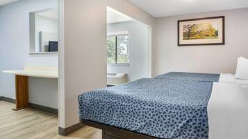 A hotel room with a bed, a bedside table, a mirror, a window, and a framed picture on the wall.