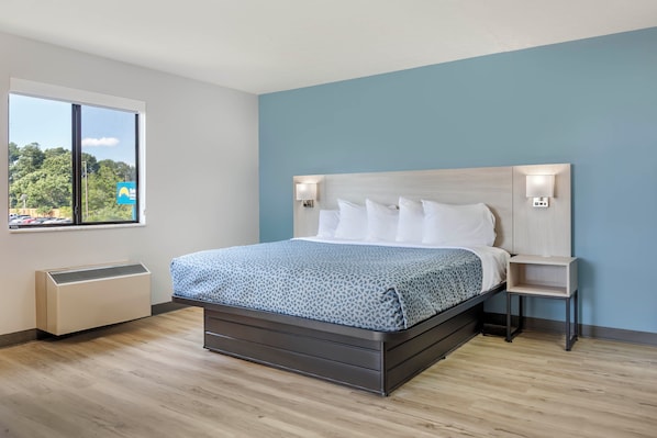 A modern hotel room with a bed, a nightstand, a window with a view, and a wall-mounted heater.