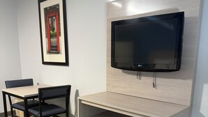 Ein gemütlicher Raum mit einem Bett, einem Nachttisch, einem an der Wand befestigten Fernseher und einem gerahmten Bild.