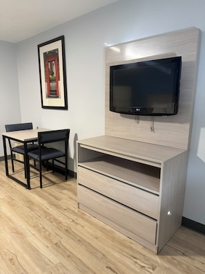 A compact room with a bed, a bedside table, a TV mounted on the wall, and a framed picture on the wall.