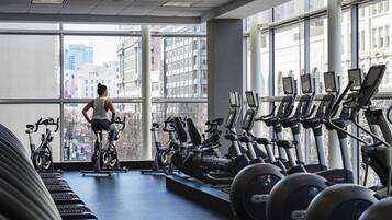 Un gimnasio con bicicletas estáticas, cintas de correr, ventanas amplias y vista a la ciudad.