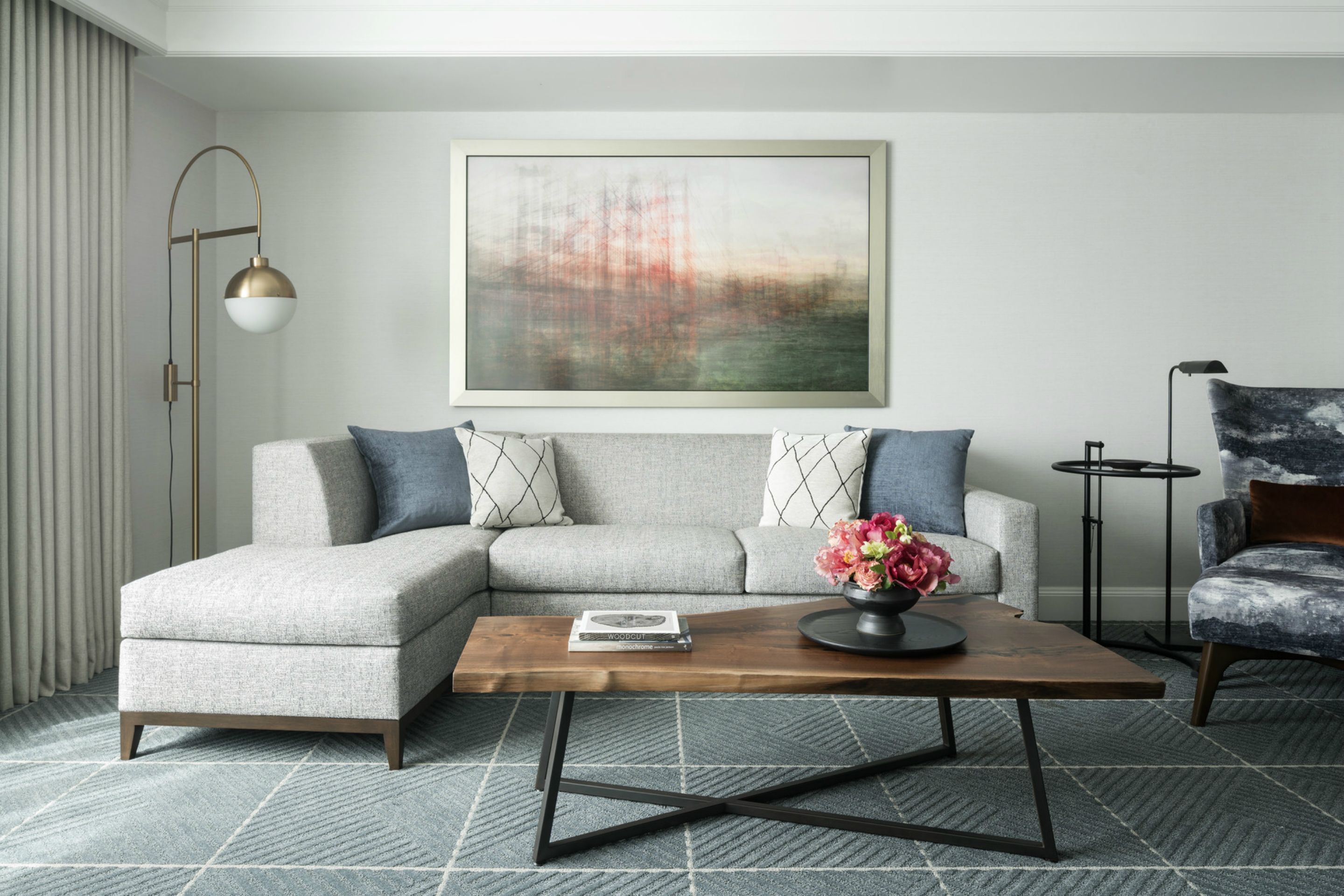 A modern living room with a sectional sofa, a coffee table, a floor lamp, and a painting on the wall.