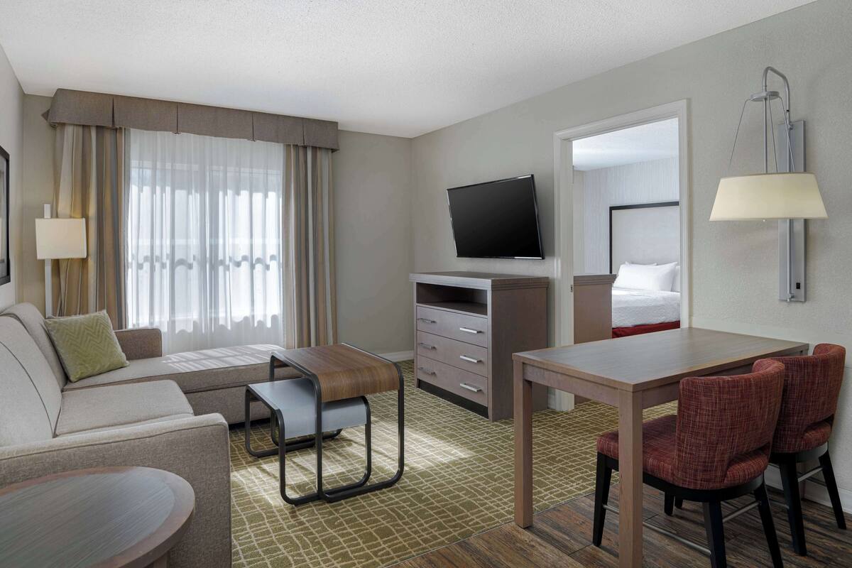 Een hotelkamer met een bank, een eettafel, een televisie, een bureau met stoelen en een bed.