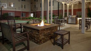 An outdoor patio with a stone fire pit, wooden chairs, and a grill.