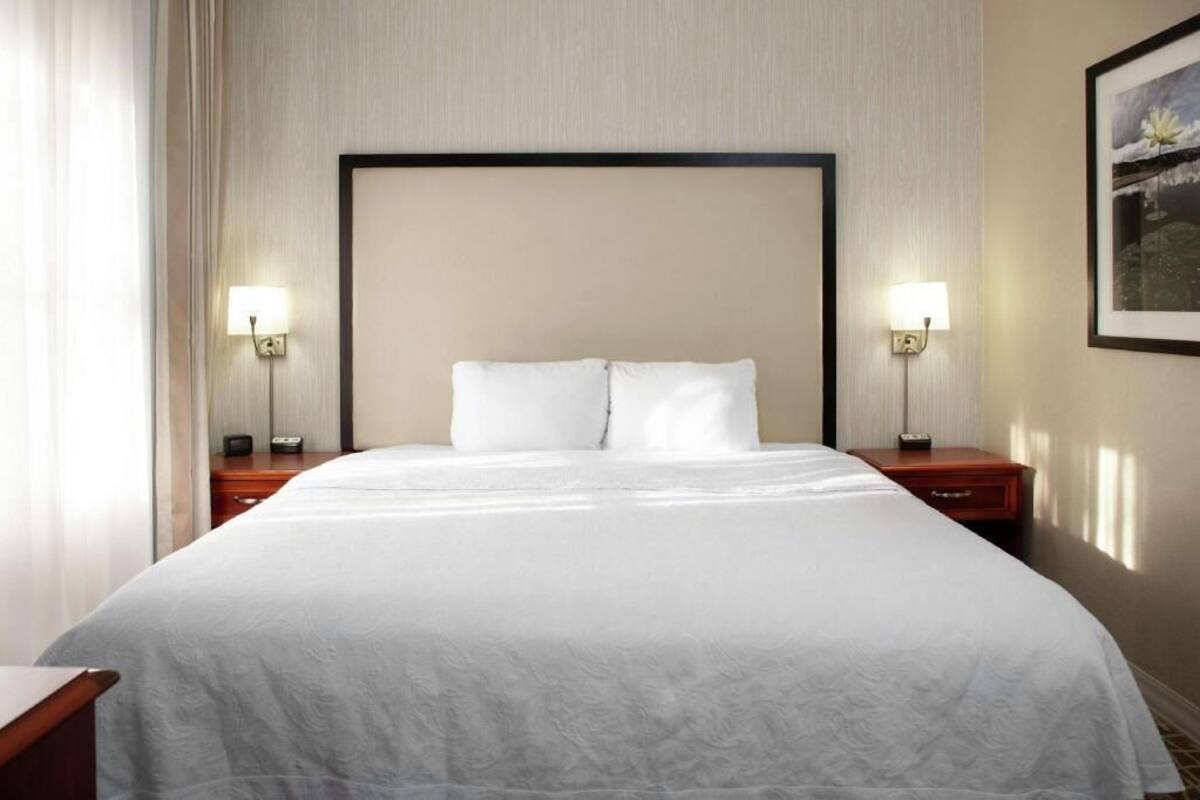 Een hotelkamer met een groot bed, twee nachtkastjes en een ingelijst kunstwerk aan de muur.