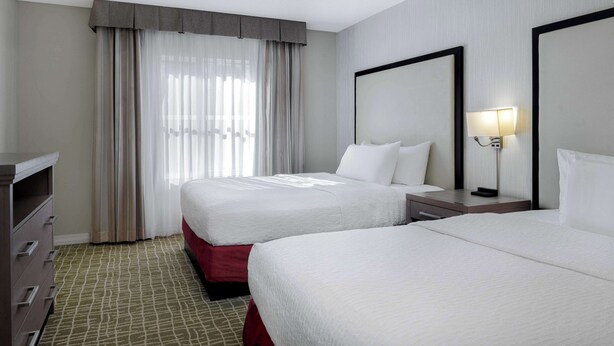 A hotel room with two beds, a dresser, a nightstand with a lamp, and a large mirror.