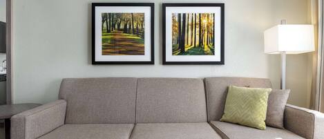 A neutral-toned sofa with a single green pillow, a wooden coffee table, and two framed pictures of forest scenes on the wall.