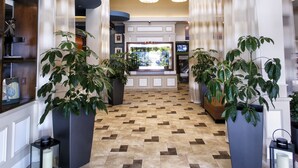 A hotel lobby with a check-in counter, potted plants, and a tiled floor.