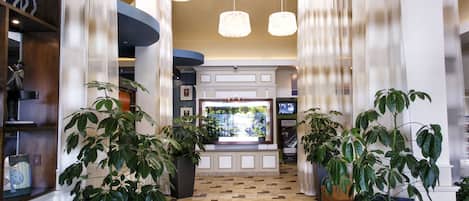A hotel lobby with a check-in counter, potted plants, and a tiled floor.
