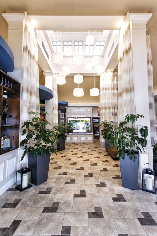 Een hotel lobby met een receptiebalie, planten in potten en een betegelde vloer.