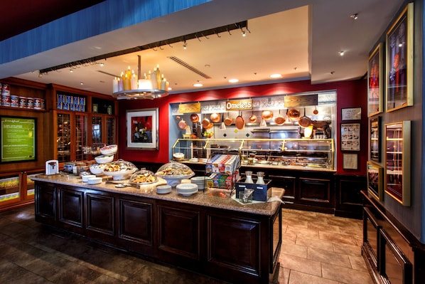 Ein Bereich mit Buffet, einer Auswahl an Speisen, einer Kaffeestation und einem Schild mit der Aufschrift 'Omeletts'.