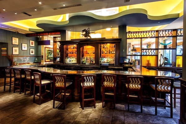 A bar area with a curved counter, multiple bar stools, and a variety of bottles and glasses.