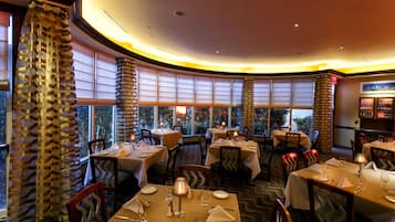 Un restaurant avec des tables et des chaises rondes, de grandes fenêtres et un tapis à motifs.