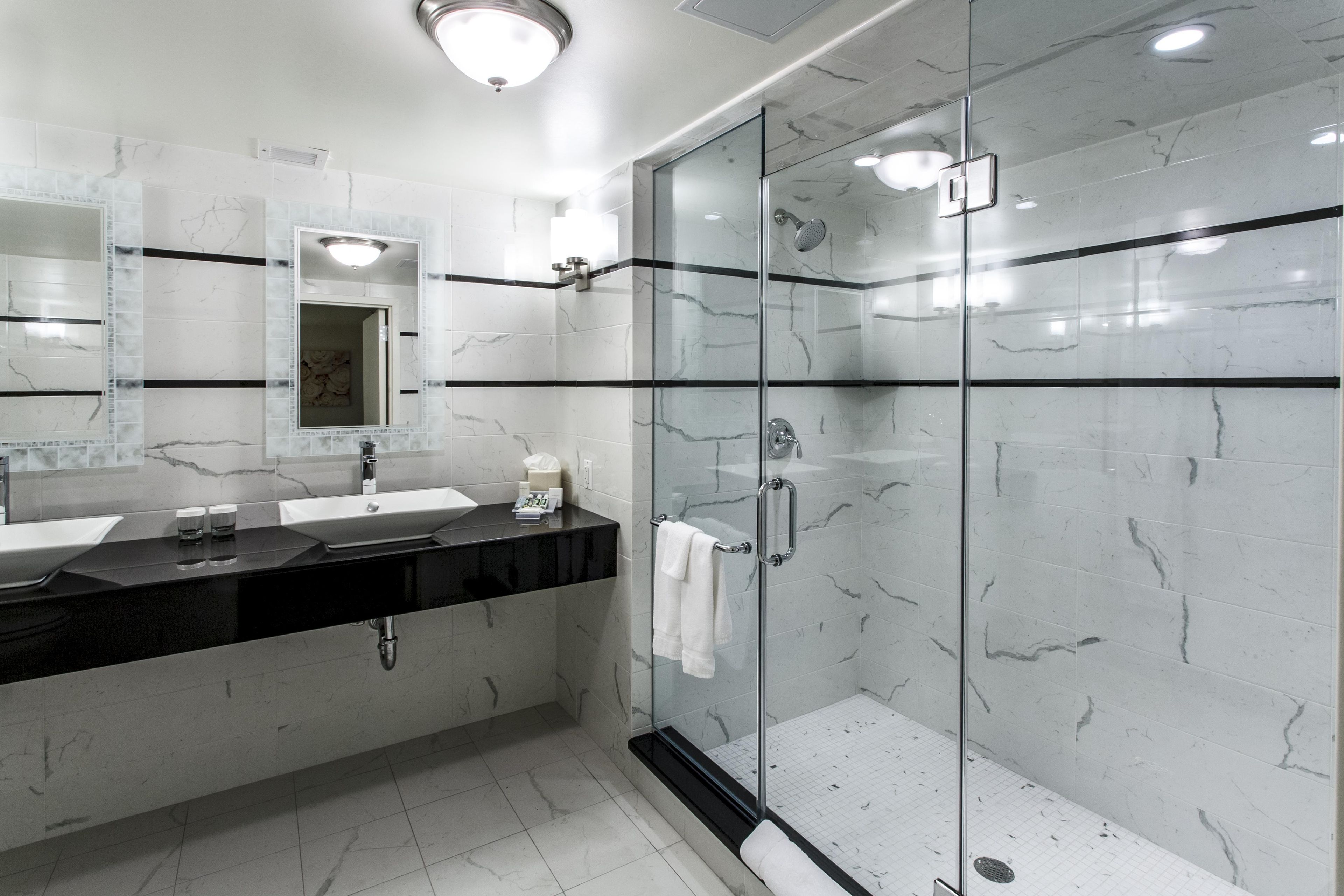 A modern bathroom with a glass-enclosed shower, a large mirror, and a black countertop.
