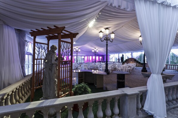 Un espacio para eventos al aire libre con carpas, mesas, sillas, una estatua y una pérgola.