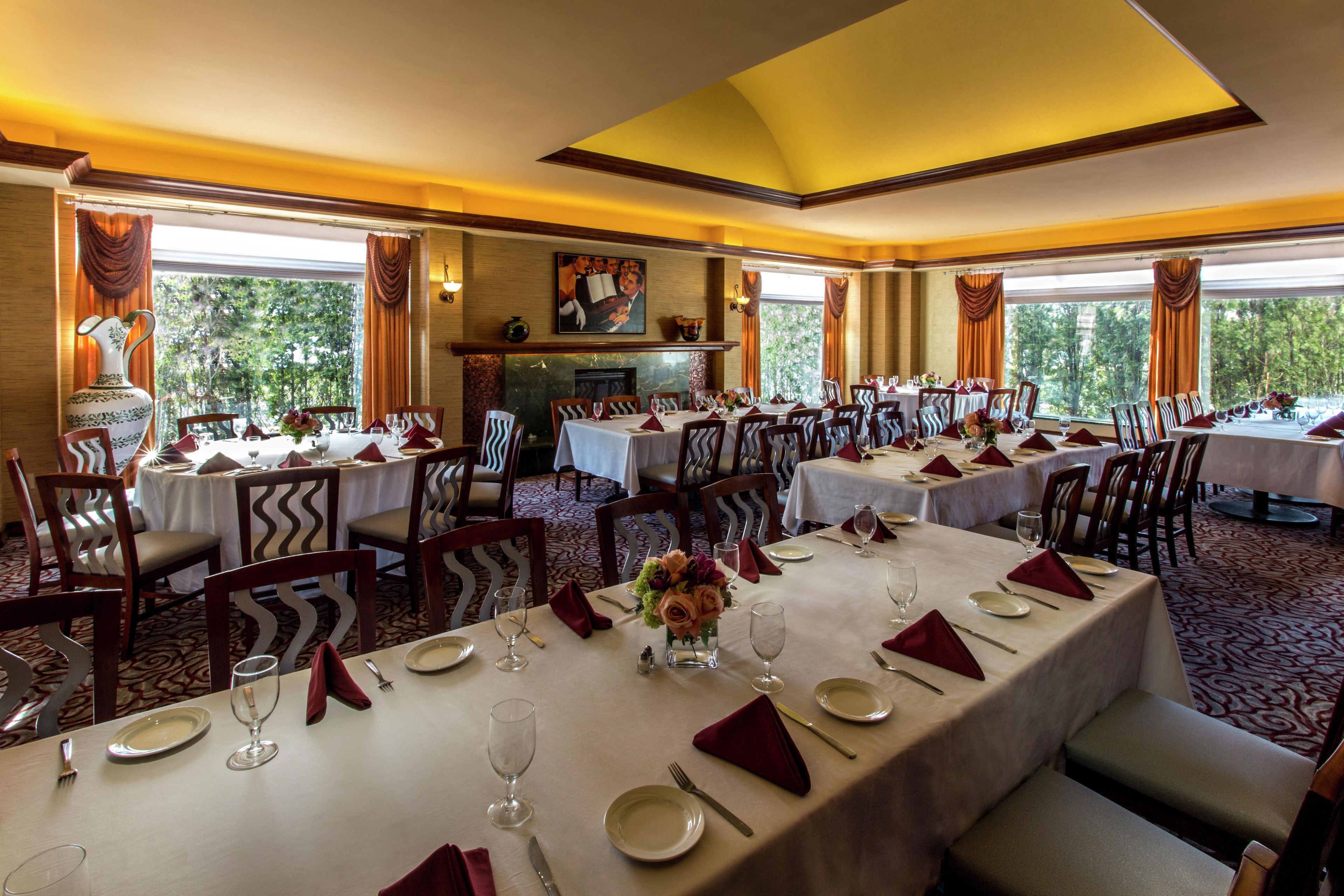 A restaurant with multiple tables set for dining, featuring a view of greenery outside.