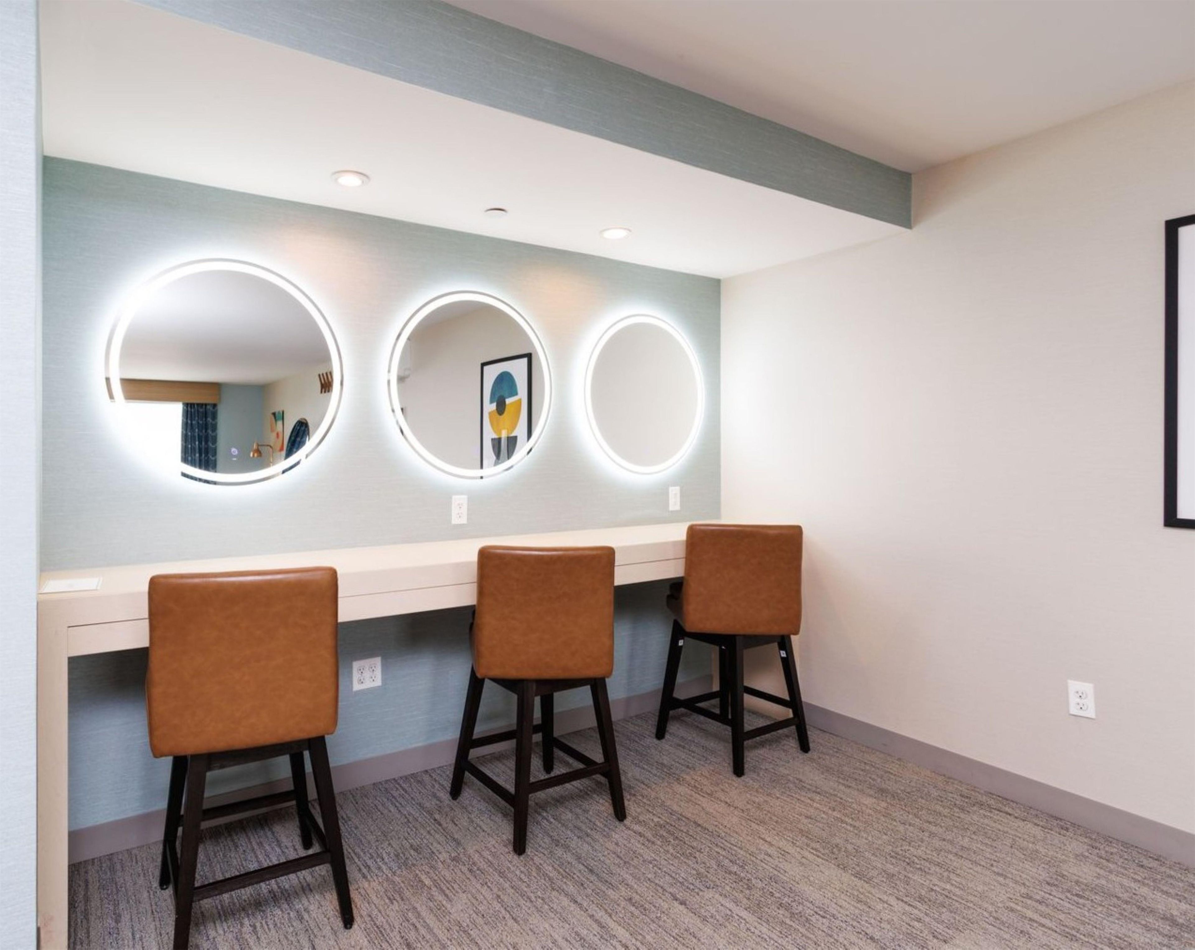 A room with three stools and three illuminated mirrors on a wall.