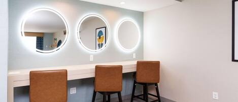A room with three stools and three illuminated mirrors on a wall.