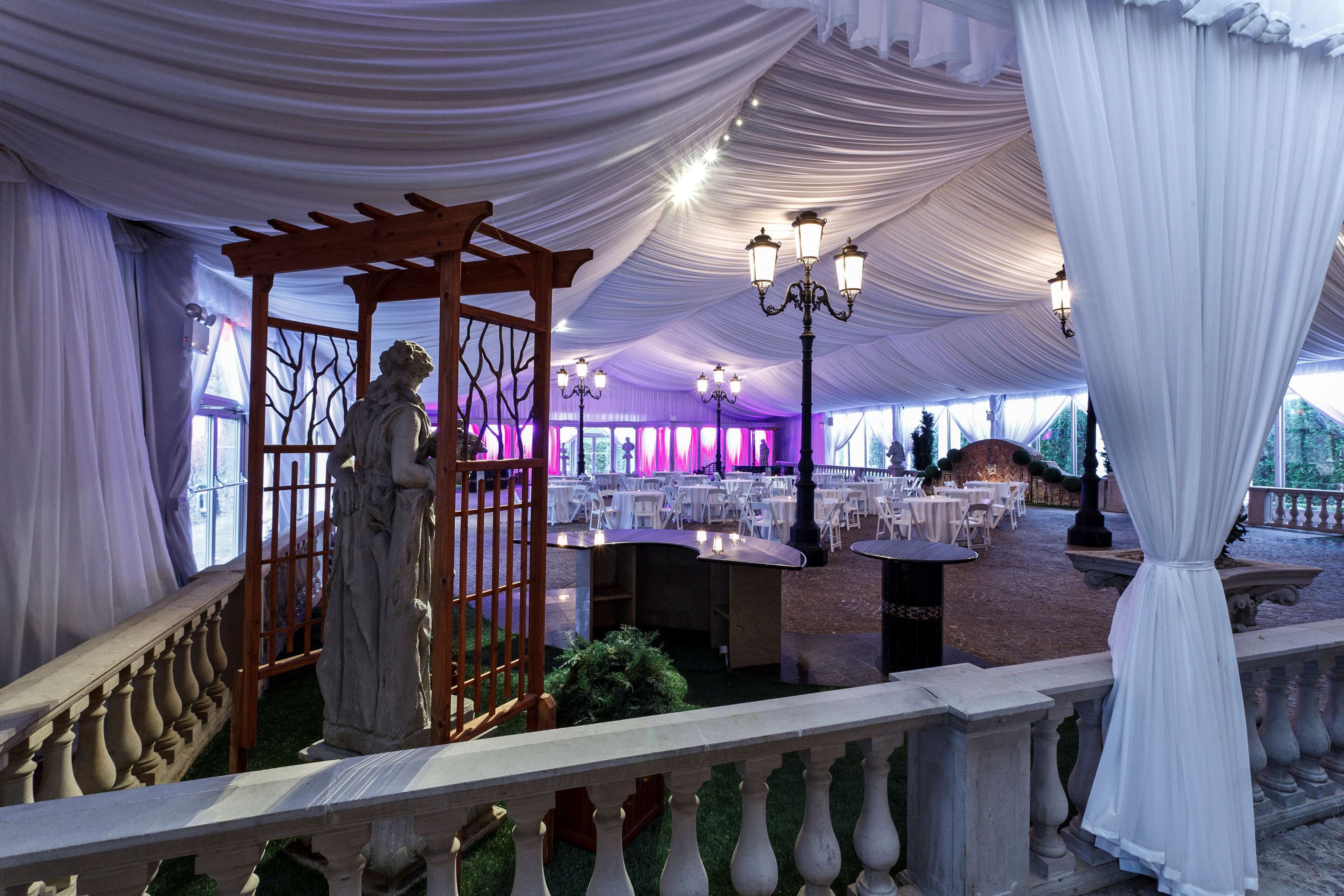 Un espacio para eventos al aire libre con carpas, mesas, sillas, una estatua y una pérgola.