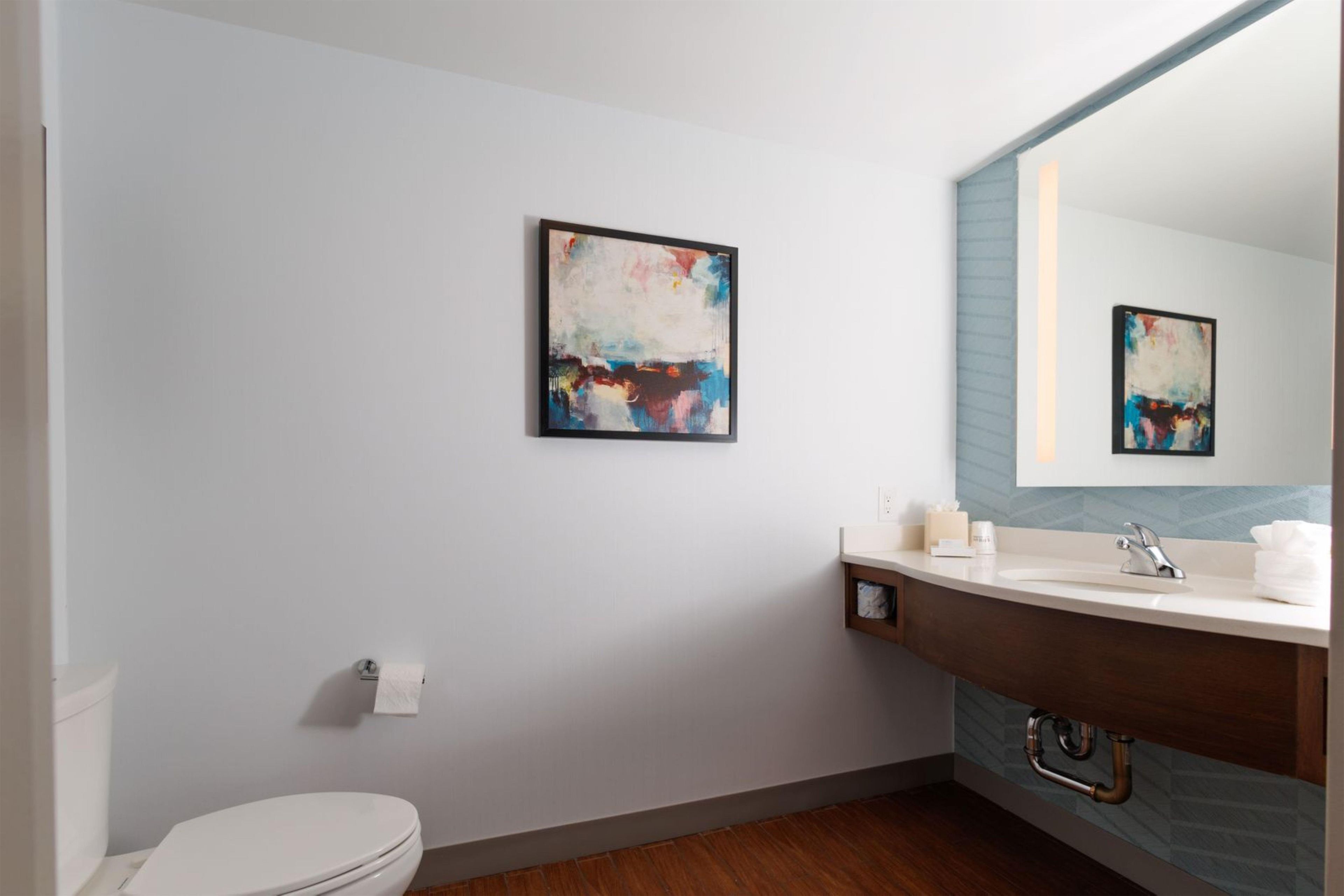 Un baño moderno con inodoro, lavamanos y dos cuadros abstractos en la pared.